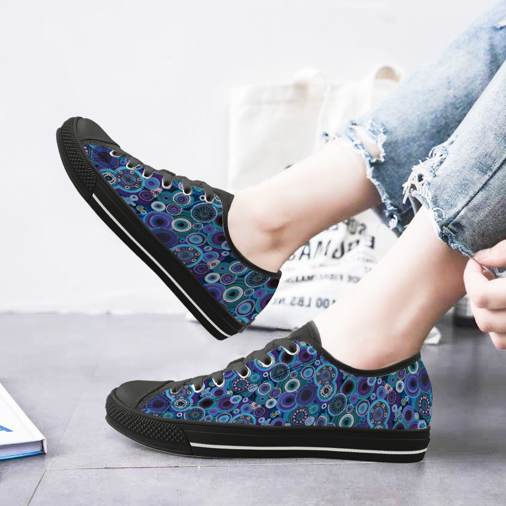 Sneakers with black features and painted with thosands of interlocking circles of purple and teal. with model