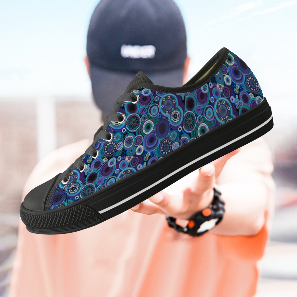 Sneakers with black features and painted with thosands of interlocking circles of purple and teal., with model